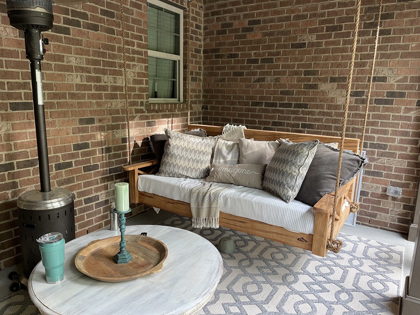 Twin bed swing with neutral patterned pillows on a brick porch