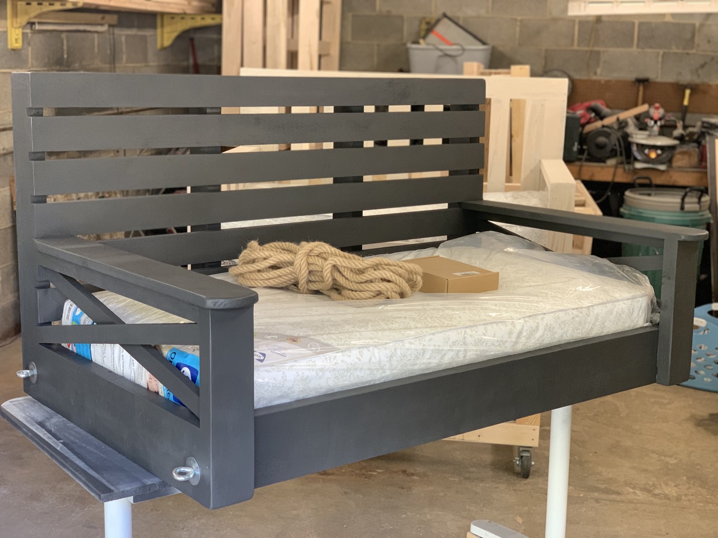 Charcoal-painted bed swing frame with mattress in the workshop