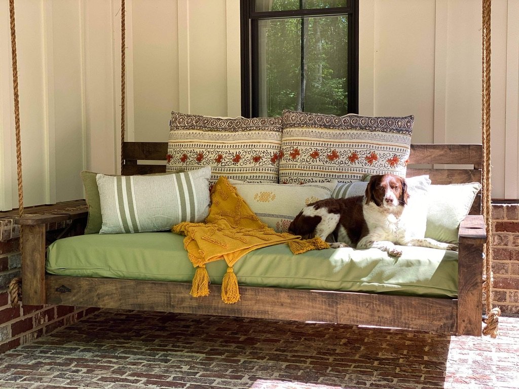Porch swing with dog and green cushions