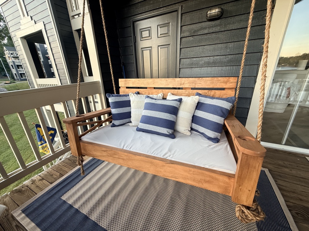Honey-stained bed swing with navy striped pillows on a lake house porch