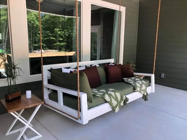 White crib-size bed swing hanging on a covered porch